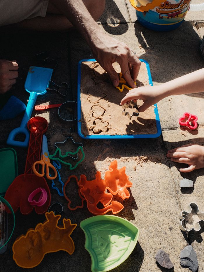A father and child enjoy creating sand shapes using colorful molds outdoors.
