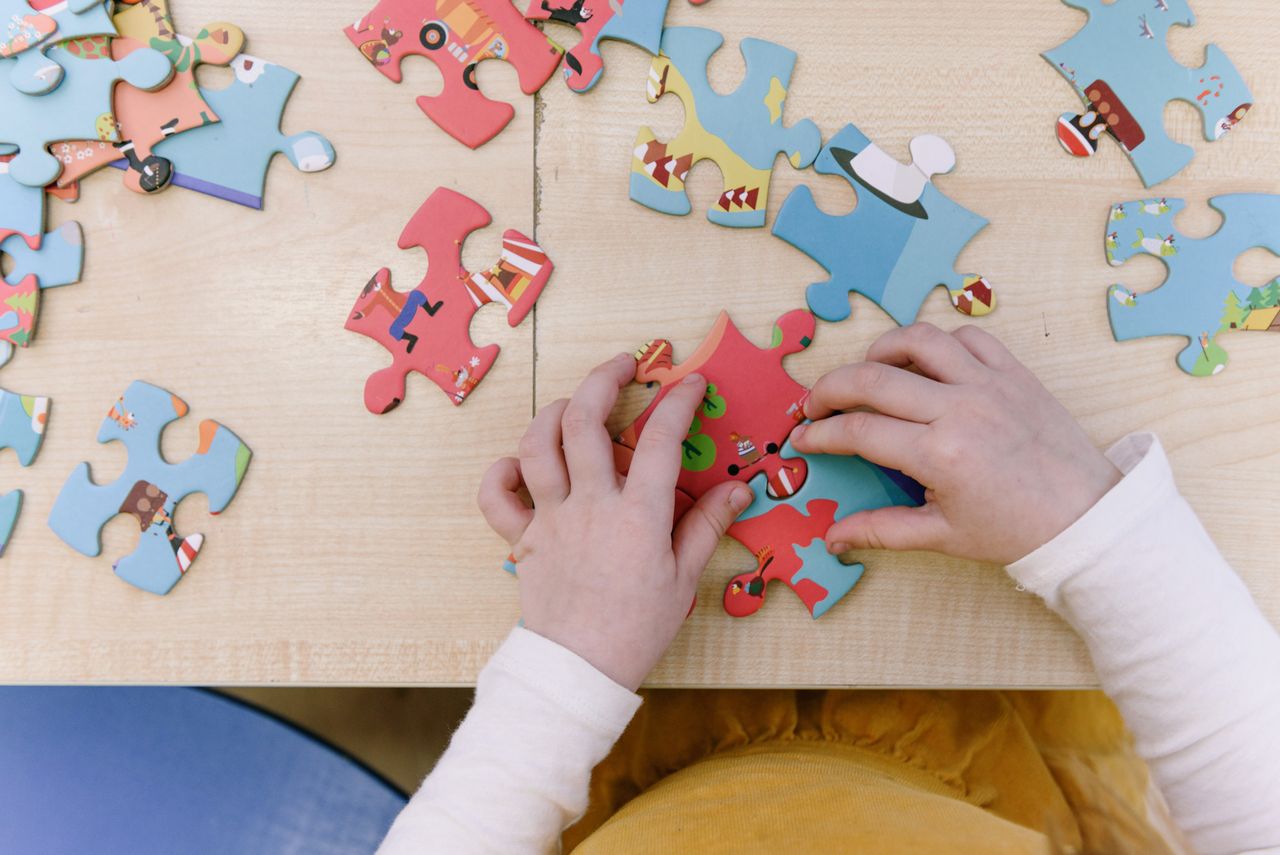 Home Close-up of child assembling colorful puzzle pieces on a wooden table, top view.